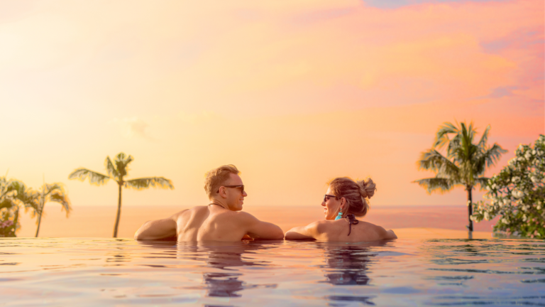 Couple relaxing in an infinity pool with a stunning sunset view and palm trees, highlighting the serene beauty of Bali, a top destination for 2025.