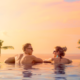 Couple relaxing in an infinity pool with a stunning sunset view and palm trees, highlighting the serene beauty of Bali, a top destination for 2025.